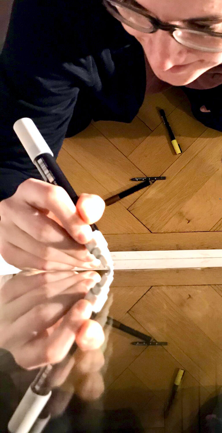 Das Bild zeigt Schilderbilder beim Beschriften eines Fensters mit einem Akrylstift. Es liegt eine Kreide am Boden und weitere Kreidestifte.